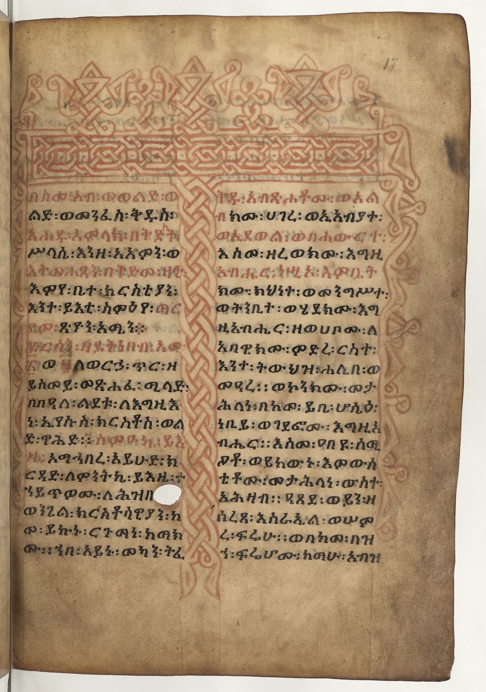A page from an Ethiopian manuscript on cream-coloured parchment, written in two columns of Geʽez in dense black ink with whole words and phrases picked out in red. Across the top runs a harag — a broad band of red interlace, woven like basketwork, crowned with a row of looped and knotted finials — and a narrower column of the same interlace runs the full height of the page down the gutter between the two text columns, with red tendrils curling out into the right margin. A small round hole in the parchment sits in the lower left column, and the scribe has simply written around it. The page is numbered 17 in pencil at the top right; the edges are worn and faintly stained.